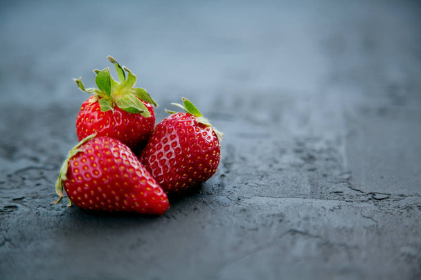 Close-up three red fresh juicy strawberries on a dark background - Fotoğraf, Görsel