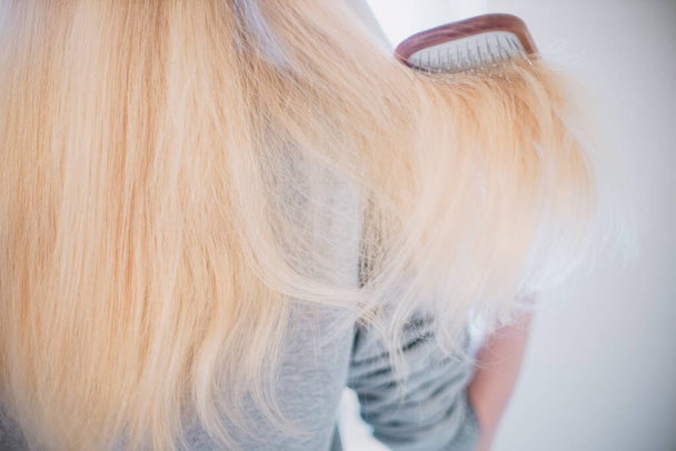 Jovem penteando longos cabelos loiros com um pente de madeira, visão traseira, close-up
 - Foto, Imagem