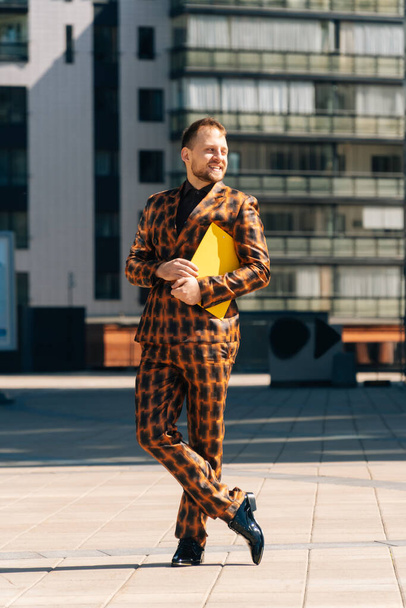 Vertical frame of a handsome young man in an official orange suit with a yellow folder in his hands.Straight frame concept in stylish clothes. - Фото, изображение