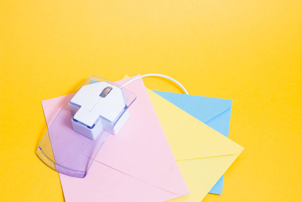 transparent plastic computer mouse and paper colored envelopes on a yellow background, copy space, online communication and sending gifts over the Internet - Φωτογραφία, εικόνα
