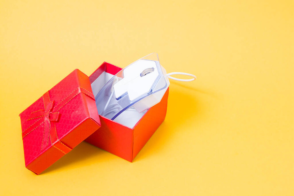 online shopping concept, computer mouse made of transparent plastic in a red coat box with a bow, yellow background, copy space, buying a gift on the Internet - Φωτογραφία, εικόνα