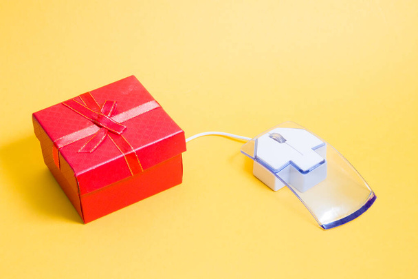 online shopping concept, transparent plastic computer mouse and red bow-tie box, yellow background, copy space, buying a gift on the Internet - Valokuva, kuva