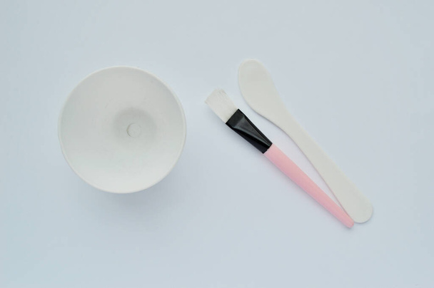 миска, щетка и лопатка для изготовления маски для лица на белом фоне. Спа дома
 - Фото, изображение