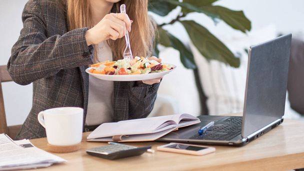 Mujer de negocios joven irreconocible teniendo una pausa para comer en el escritorio, ella está comiendo ensalada fresca, persona
 - Foto, imagen