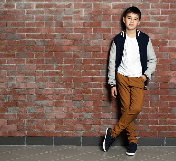 Tatlı küçük çocuk tuğla duvarın yanında duruyor. - Fotoğraf, Görsel