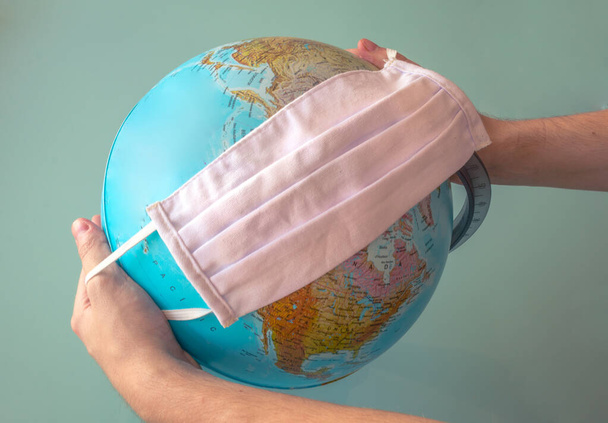 Hände, die eine Gesichtsmaske um die Erde halten. Das heißt, die Erde benutzt Maske für die Umweltverschmutzung, ein Virus usw. - Foto, Bild