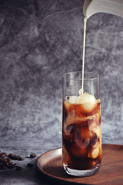 Льодову каву у високій склянці з вершками наливають і кавові зерна на стару сільську дерев'яну дошку. Холодний літній напій на темному дерев'яному фоні з копіювальним простором
 - Фото, зображення