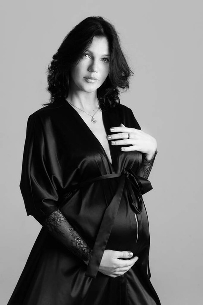 Portrait shoot of young beautiful pregnant woman posing for maternity photoshoot lifestyle, pregnant belly. Stylish happy mother wearing a black elegant robes and to be waiting for a baby  - Photo, image