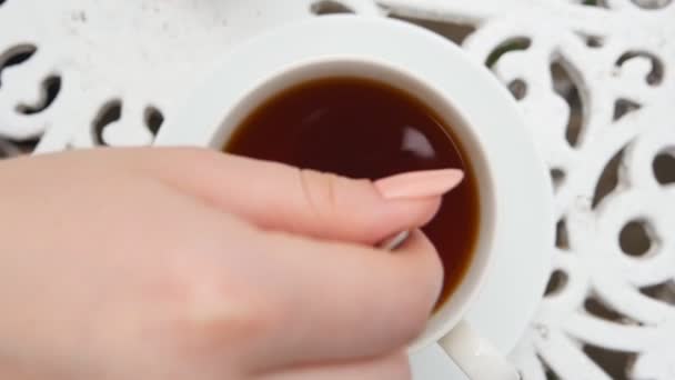La mano femenina sostiene una cuchara de metal y revuelve el azúcar o stevie en una taza blanca con un té de hierbas. Mujer joven prepara una bebida caliente saludable en el desayuno. Concepto de tranquilidad y relax. Vista superior cámara lenta
 - Metraje, vídeo