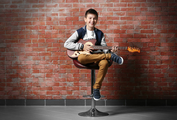 Cute little boy gra na gitarze cegły tle ściany - Zdjęcie, obraz