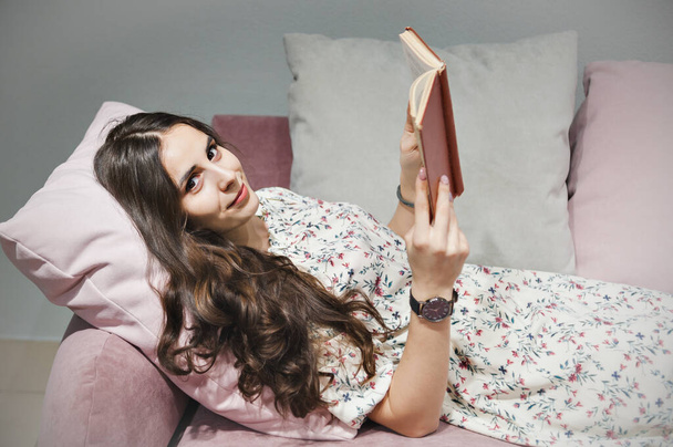 Pretty woman sitting on cozy sofa and reading book - Фото, зображення