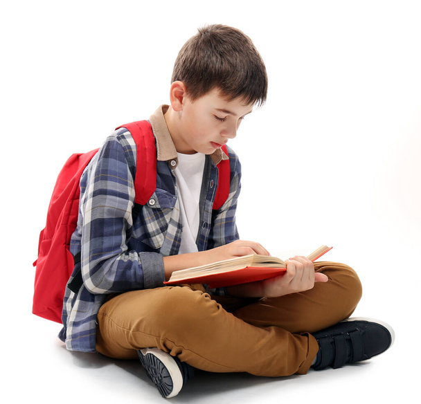 Cute little boy with red backpack reading a book, isolated on white - Φωτογραφία, εικόνα