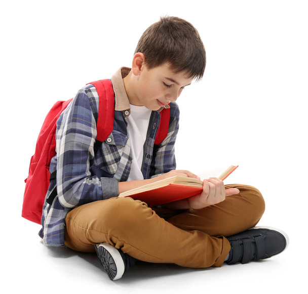 Lindo niño pequeño con mochila roja leyendo un libro, aislado en blanco
 - Foto, Imagen