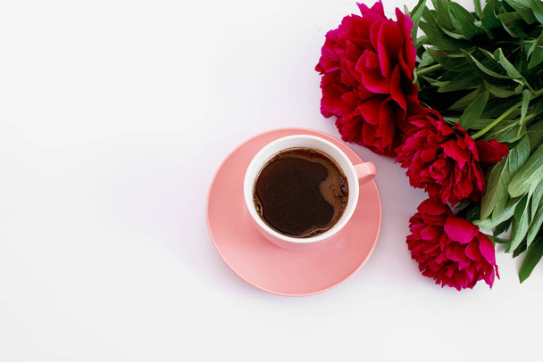 rózsaszín csésze kávé és három piros bazsarózsa a fehér háttér - Fotó, kép