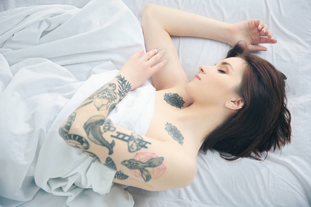 Vonzó nő tetoválással az ágyon - Fotó, kép