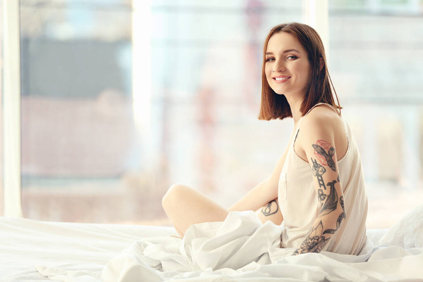 Ελκυστική γυναίκα με τατουάζ κάθεται στο κρεβάτι - Φωτογραφία, εικόνα