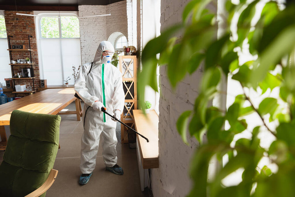 Coronavirus-Pandemie. Ein Desinfektor in Schutzanzug und Maske sprüht Desinfektionsmittel in Haus oder Büro - Foto, Bild
