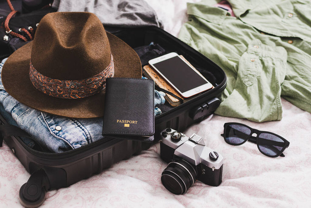 offener Koffer mit Pass, Fotokamera, Hut, Brille und Kleidung - Foto, Bild