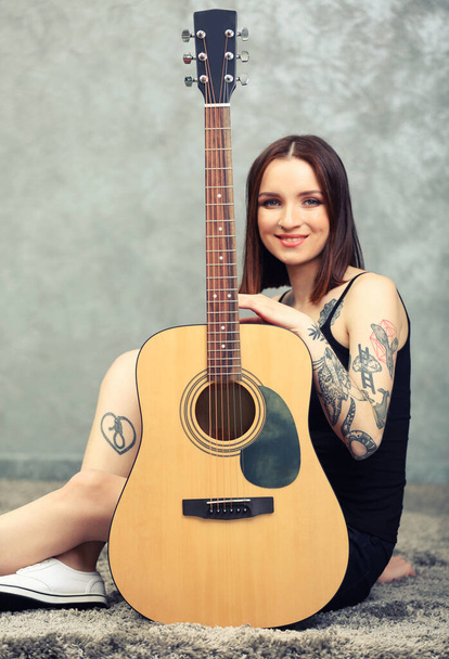 Femme avec tatouage et guitare assise sur fond gris
 - Photo, image