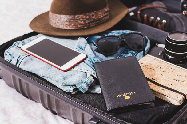 otwarta walizka z paszportem, aparatem fotograficznym, kapeluszem, okularami i ubraniami - Zdjęcie, obraz