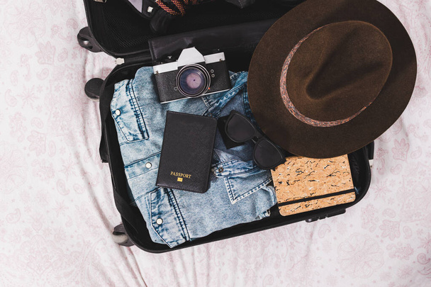 otwarta walizka z paszportem, aparatem fotograficznym, kapeluszem, okularami i ubraniami - Zdjęcie, obraz