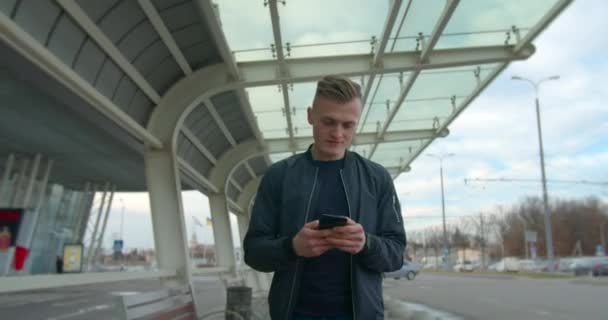 The guy is typing the message when he passing the airport and looking for transport. 4K - Séquence, vidéo