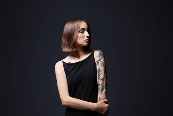Όμορφη νεαρή γυναίκα με τατουάζ ποζάροντας σε γκρι φόντο - Φωτογραφία, εικόνα
