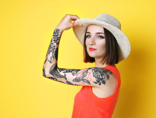 Gyönyörű fiatal nő tetovált kalapot visel, és pózol a sárga háttér - Fotó, kép