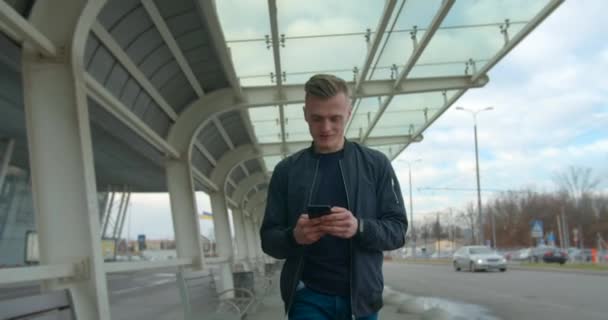 The guy is typing the message when he passing the airport and looking for transport. Beautiful smile. 4K - Materiał filmowy, wideo