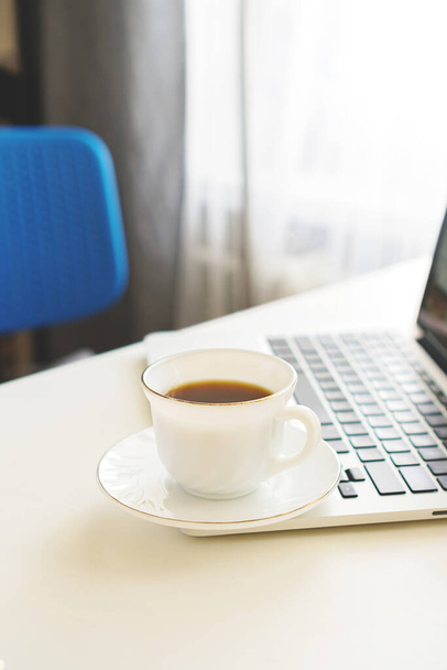coffee mug and laptop stand on the desktop on a sunny day - Фото, изображение