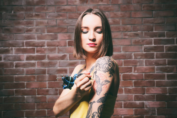 Beautiful young woman tattooing herself on brick wall background - Photo, Image