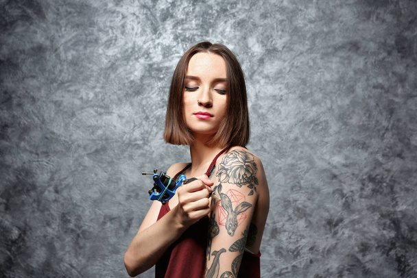 Hermosa joven tatuándose sobre fondo gris
 - Foto, Imagen