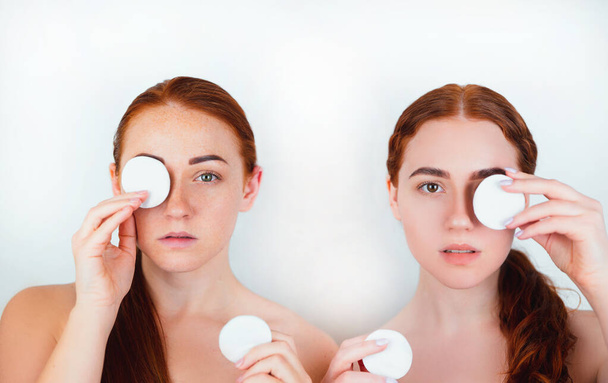 portrait of two redheaded young women looking natural both removing eye makeup with cotton pads standing on isolated white background, care and beauty concept. - Photo, Image