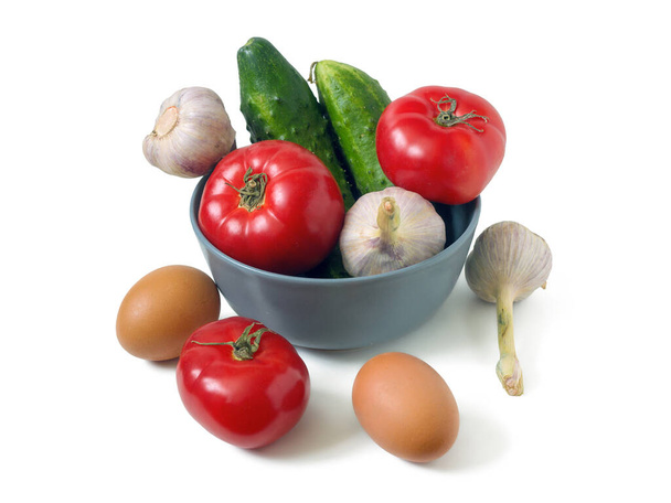 Rajčata, okurky, česnek a dvě vejce. Zelenina v šedé míse a kolem ní, izolované na bílém pozadí - Fotografie, Obrázek