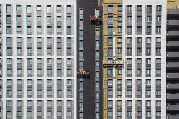 Les travailleurs dans trois berceaux de bâtiment travaillent en hauteur, finissent la façade du bâtiment de l'hôtel. Travaux en haute altitude
 - Photo, image