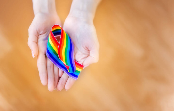 mano sostiene un arco iris de cintas LGBT sobre un fondo LUZ. Copia espacio para texto. El concepto de homosexuales y personas LGBT
. - Foto, imagen