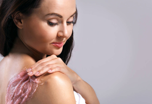 Młoda kobieta stosująca peeling na ramieniu na szarym tle - Zdjęcie, obraz