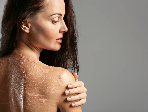 Νεαρή γυναίκα εφαρμογή scrub στον ώμο σε γκρι φόντο - Φωτογραφία, εικόνα