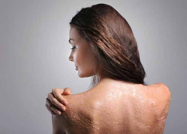 Jovem mulher aplicando esfoliação no ombro no fundo cinza
 - Foto, Imagem