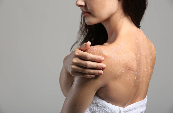 Νεαρή γυναίκα εφαρμογή scrub στον ώμο σε γκρι φόντο - Φωτογραφία, εικόνα