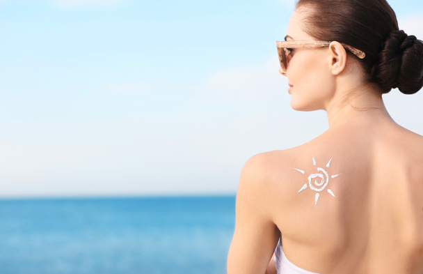 Woman with sun protective lotion in sun shape on shoulder - Photo, Image