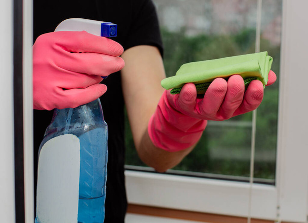mladý muž v růžových gumových rukavicích drží čistič oken a hadr a umývá plastová okna  - Fotografie, Obrázek