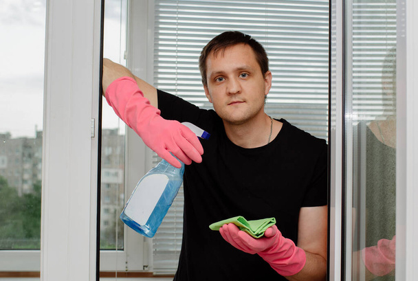 joven en guantes de goma rosa sostiene limpiador de ventanas y trapo y lava ventanas de plástico
  - Foto, Imagen
