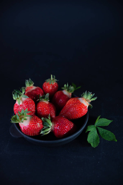 Fresh juicy strawberries in a black plate on a black matte background - Фото, зображення