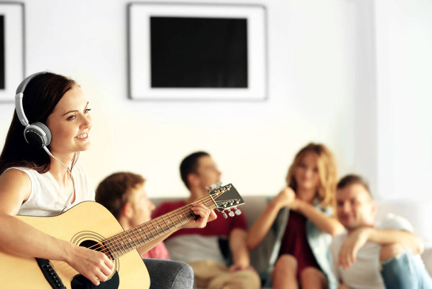 Mujer feliz tocando la guitarra y escuchando música con amigos en casa
 - Foto, imagen