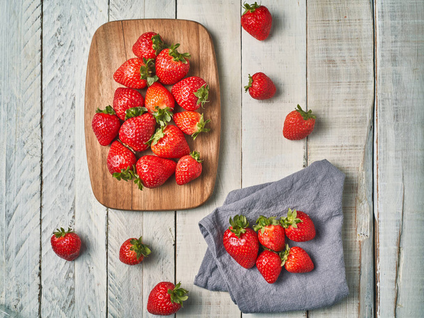 Top view of some red strawberries on a wooden board on a white table. - Photo, image