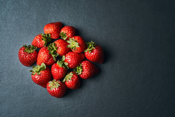 Top view of some red strawberries on a dark background. - Zdjęcie, obraz