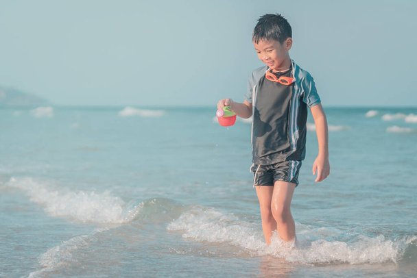 Kleine jongen speelt met golf en zand op Thailand strand - Foto, afbeelding