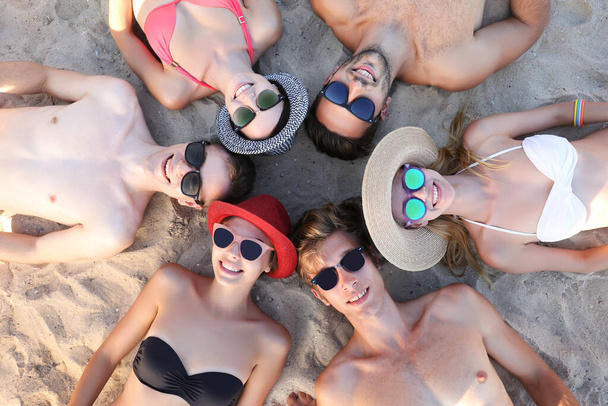 Група друзів, що лежать на пляжному піску
 - Фото, зображення