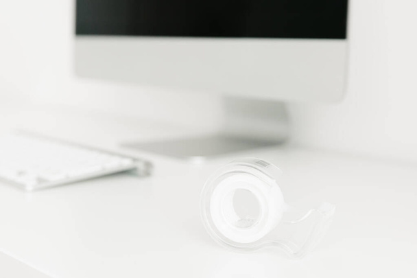 スクラッチテープディスペンサーのクローズアップは、モニターとキーボードの背景を背景にデスクトップ上にあります。文房具事務所のコンセプト - 写真・画像